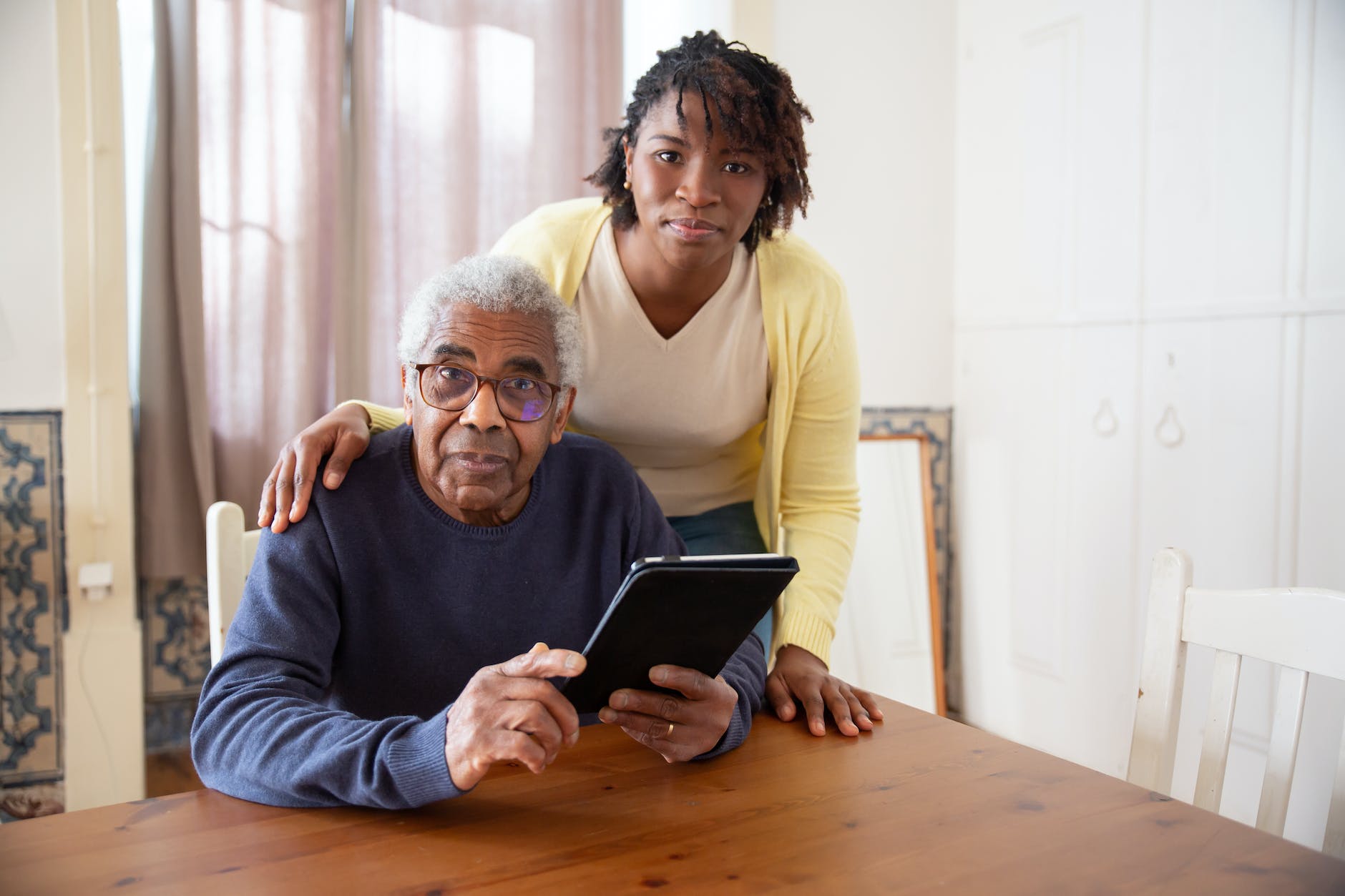 a woman standing beside the elderly man holding a tablet
