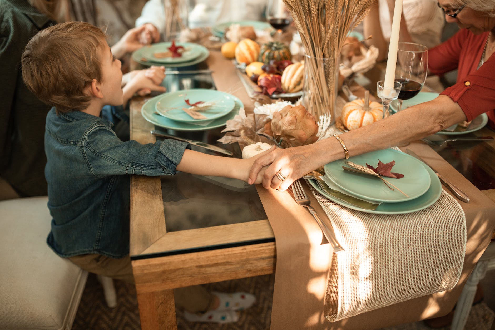 a family holding their hands praying and sitting together on a dining table
